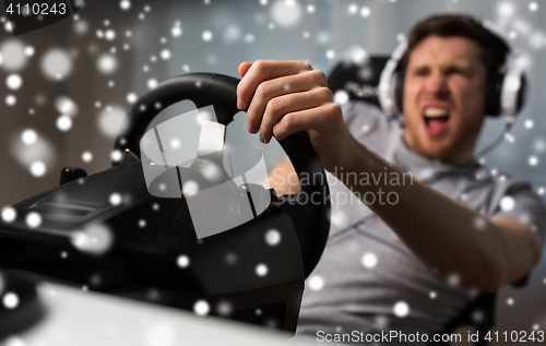 Image of man playing car racing video game with wheel