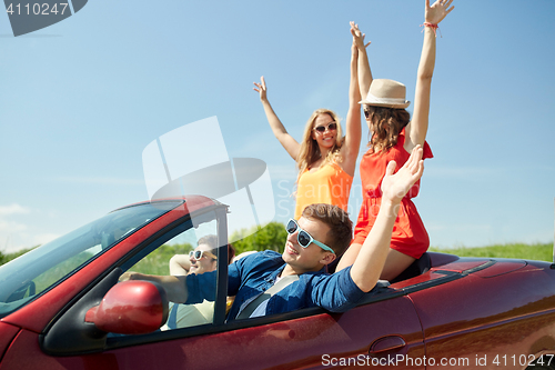 Image of happy friends driving in cabriolet car at country