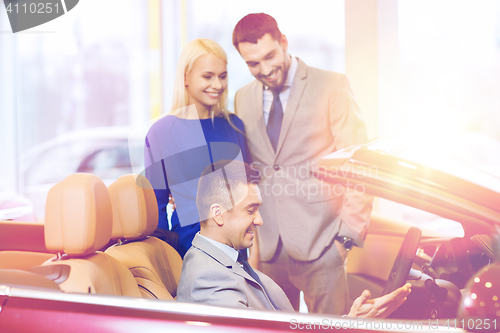 Image of happy couple with car dealer in auto show or salon