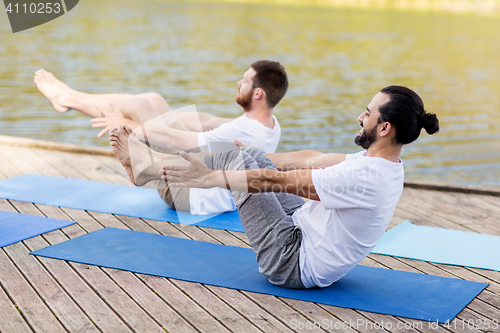 Image of men making yoga in half-boat pose outdoors