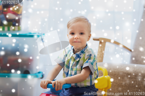 Image of happy little baby boy driving ride-on car at home