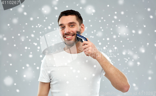 Image of smiling man shaving beard with trimmer over snow