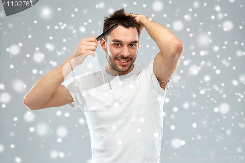 Image of happy man brushing hair with comb over snow