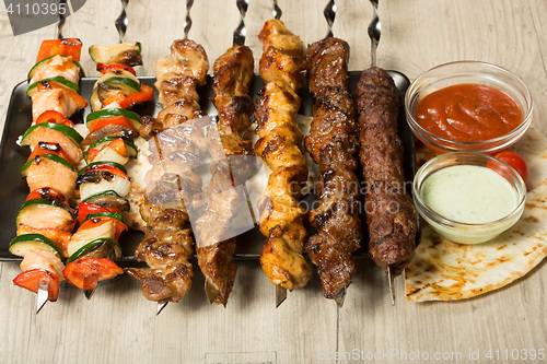 Image of set shashlik. kebab skewer, black rectangular plate. sauce and onions