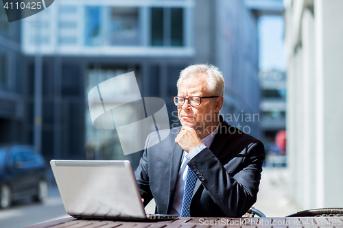 Image of senior businessman with laptop at city street cafe