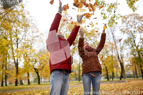 Image of happy young couple throwing autumn leaves in park