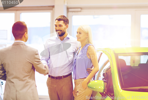 Image of happy couple with car dealer in auto show or salon