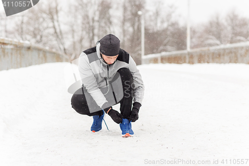 Image of man with earphones tying sports shoe in winter