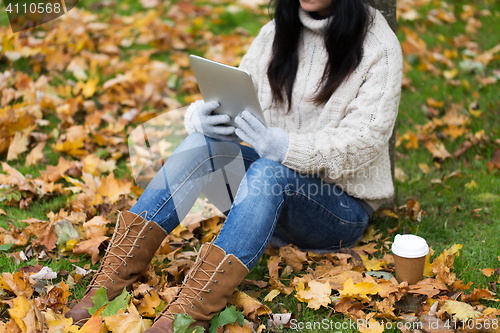 Image of woman with tablet pc and coffee in autumn park