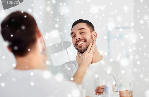 Image of happy man applying aftershave at bathroom mirror