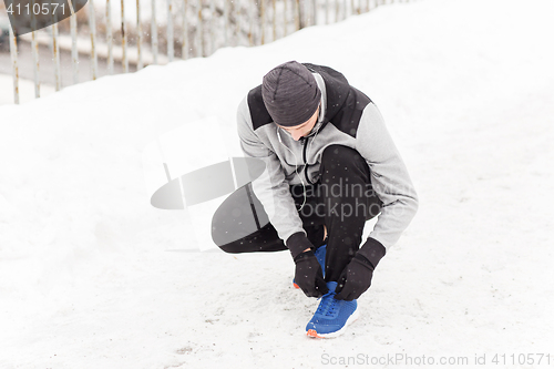 Image of man with earphones tying sports shoe in winter