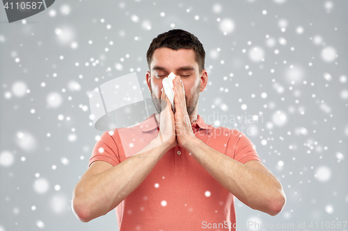 Image of sick man with paper wipe blowing nose over snow