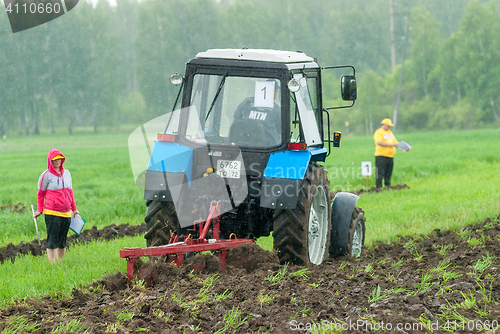 Image of Tractor operator plows the site in rain. Tyumen