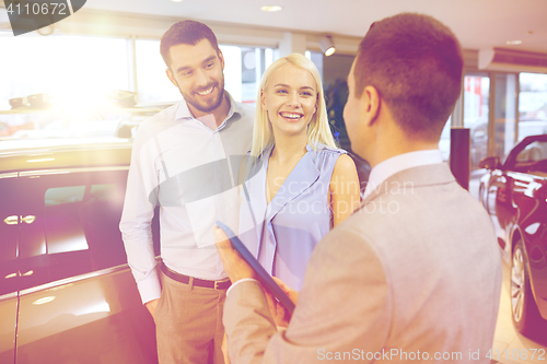 Image of happy couple with car dealer in auto show or salon