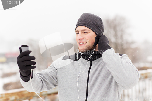 Image of happy man with earphones and smartphone in winter