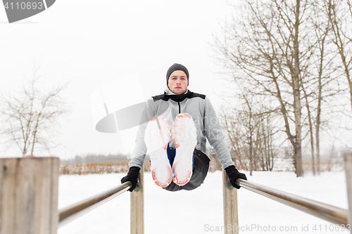 Image of young man exercising on parallel bars in winter