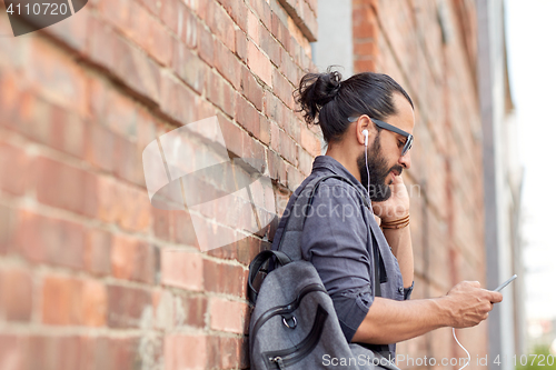 Image of man with earphones, smartphone and bag on street