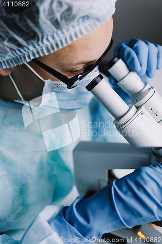 Image of Young scientist in uniform looking at microscope