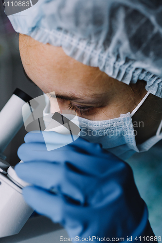 Image of Young scientist in uniform looking at microscope