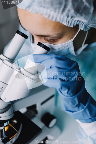 Image of Young scientist in uniform looking at microscope