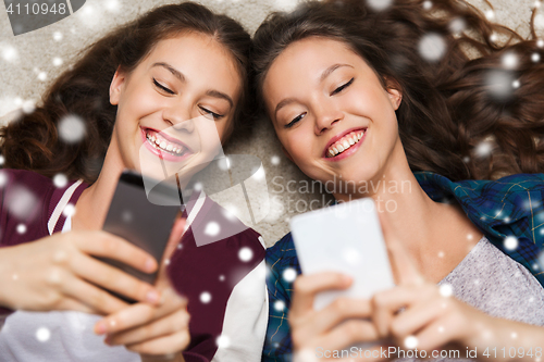 Image of happy teenage girls lying on floor with smartphone