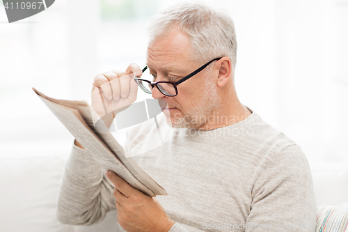 Image of senior man in glasses reading newspaper at home