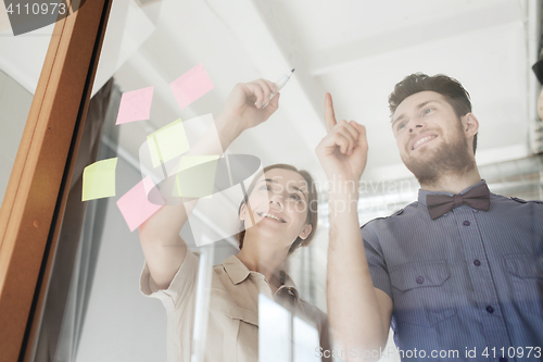 Image of happy creative team writing on blank office glass