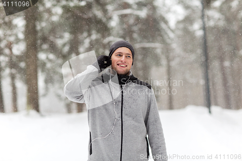 Image of happy sports man with earphones in winter forest