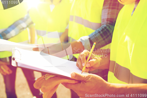 Image of close up of builders in vests writing to clipboard