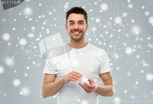 Image of happy young man with cream jar over snow