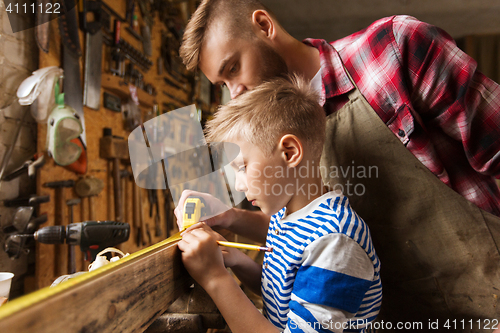 Image of father and son with ruler measure wood at workshop