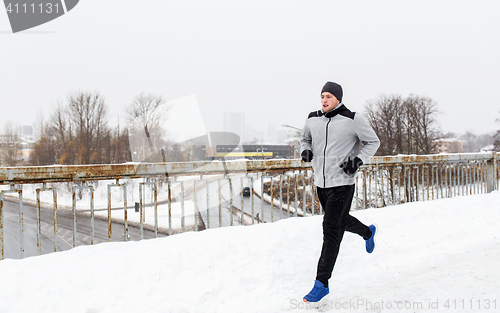 Image of man in earphones running along winter bridge