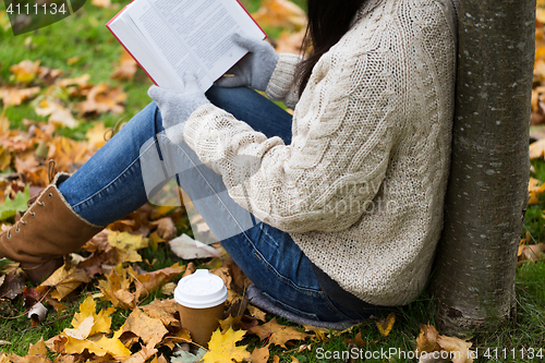 Image of woman with book drinking coffee in autumn park