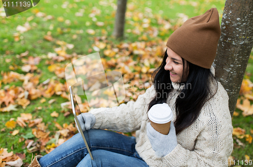 Image of woman with tablet pc and coffee in autumn park