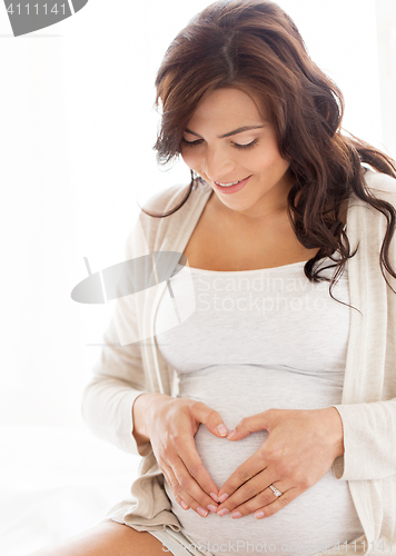 Image of happy pregnant woman making heart gesture at home