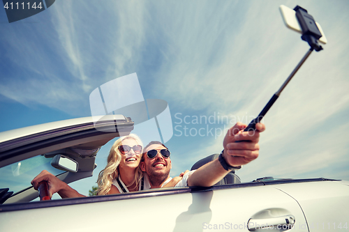Image of happy couple in car taking selfie with smartphone
