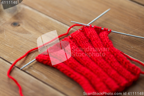 Image of hand-knitted item with knitting needles on wood