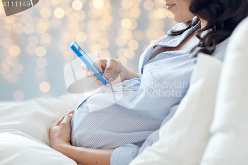 Image of close up of pregnant woman with smartphone in bed