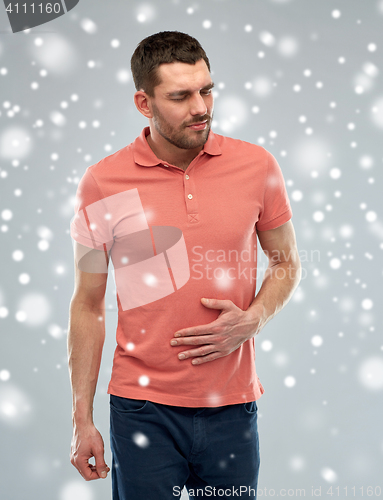 Image of unhappy man suffering from stomach ache over snow