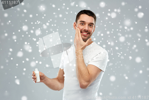 Image of happy young man applying cream or lotion to face