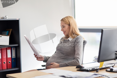 Image of pregnant businesswoman reading papers at office