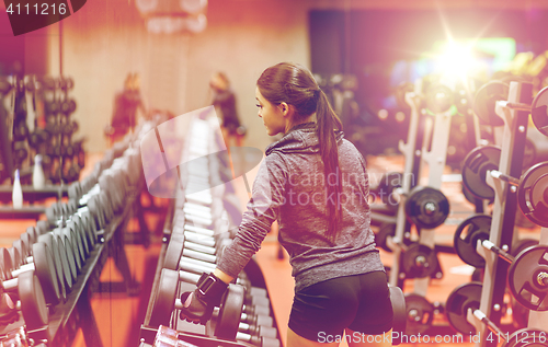 Image of young woman choosing dumbbells in gym