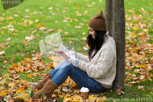 Image of woman with book drinking coffee in autumn park