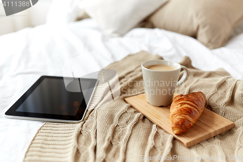 Image of tablet pc, coffee and croissant on bed at home