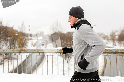 Image of man in earphones running along winter bridge