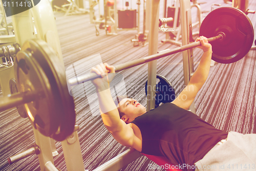 Image of young man flexing muscles with barbell in gym