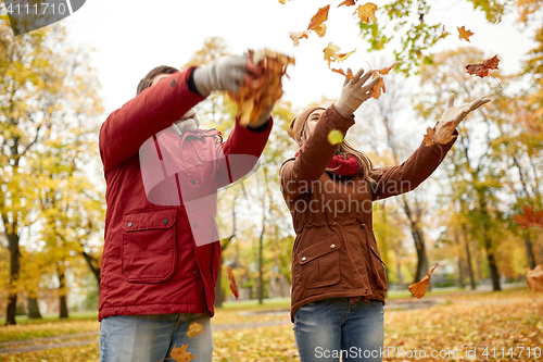 Image of happy young couple throwing autumn leaves in park