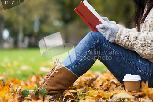 Image of woman with book drinking coffee in autumn park