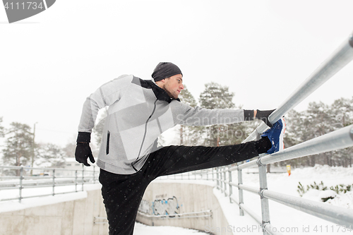 Image of sports man stretching leg at fence in winter