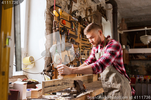 Image of carpenter working with plane and wood at workshop